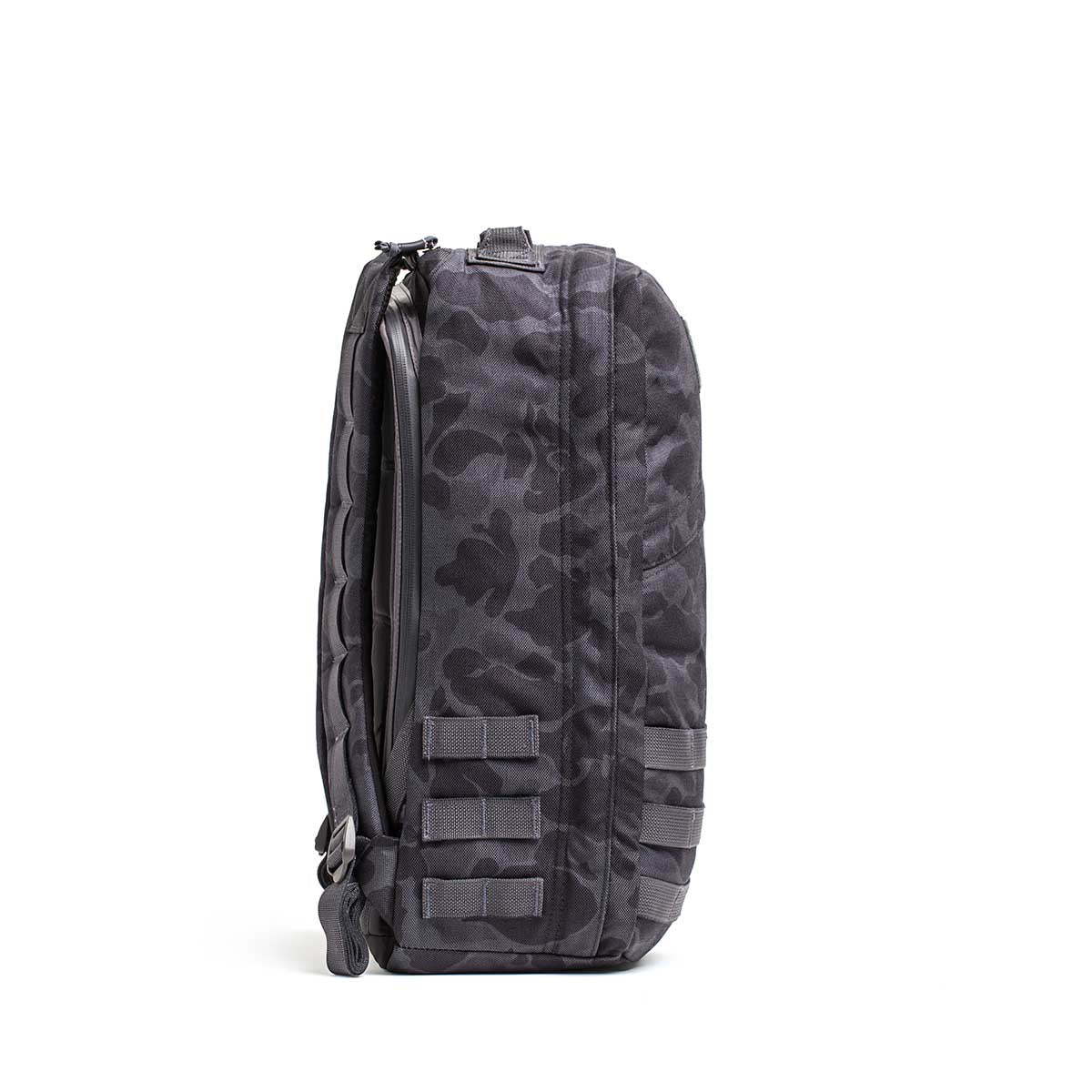 Side view of the GR1 rucksack in dark camo with multiple straps and a zipper, standing upright on white—crafted for Special Forces-grade durability and made in the USA.