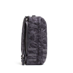 Side view of the GR1 rucksack in dark camo with multiple straps and a zipper, standing upright on white—crafted for Special Forces-grade durability and made in the USA.