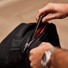 Hand placing phone in black GORUCK rucking backpack with orange interior.