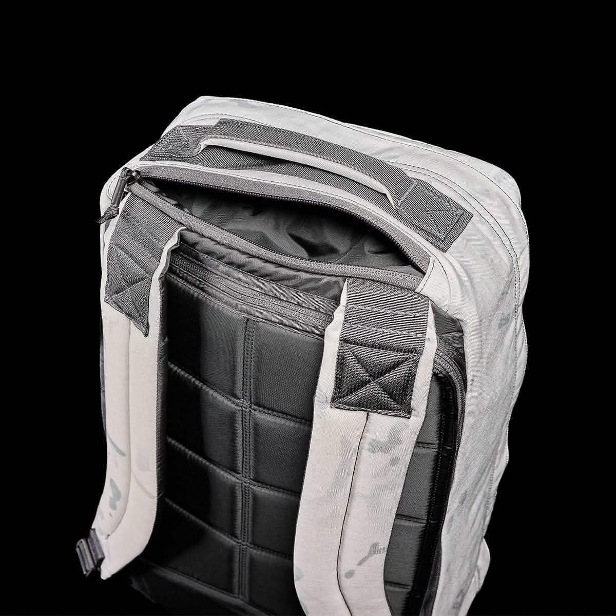 The GR1 rucksack, American made and inspired by Special Forces backpacks, features a light gray body, padded black back panel, and partially open top zipper—all shown against a black background.