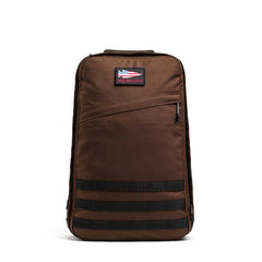 The GR1 is a brown American-made backpack featuring a small top patch, front zipper pocket, and black horizontal straps at the bottom.