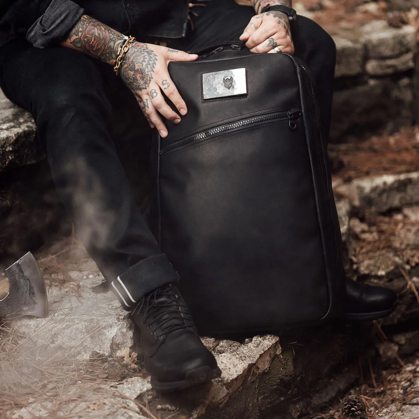 GORUCK black ruck backpack outdoors, person with tattoos, boots, and axe nearby on rocks