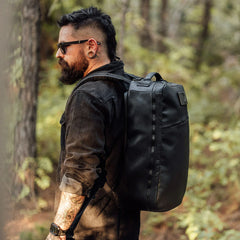 Man wearing black GORUCK rucksack outdoors in forest, showcasing rugged rucking gear
