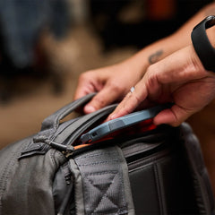 Close-up of hands placing a tablet into a GORUCK grey rucksack front pocket