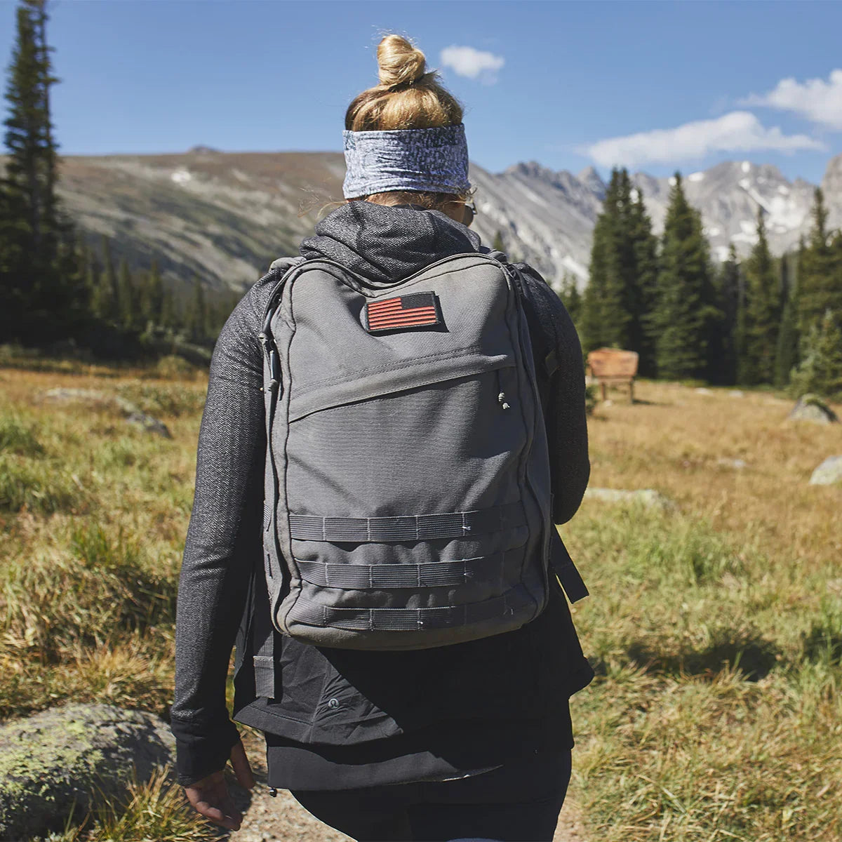 Person rucking with grey GORUCK backpack outdoors in a mountain landscape