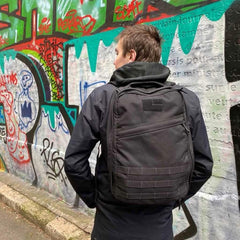 Person wearing a GORUCK backpack standing by a colorful graffiti wall outdoors