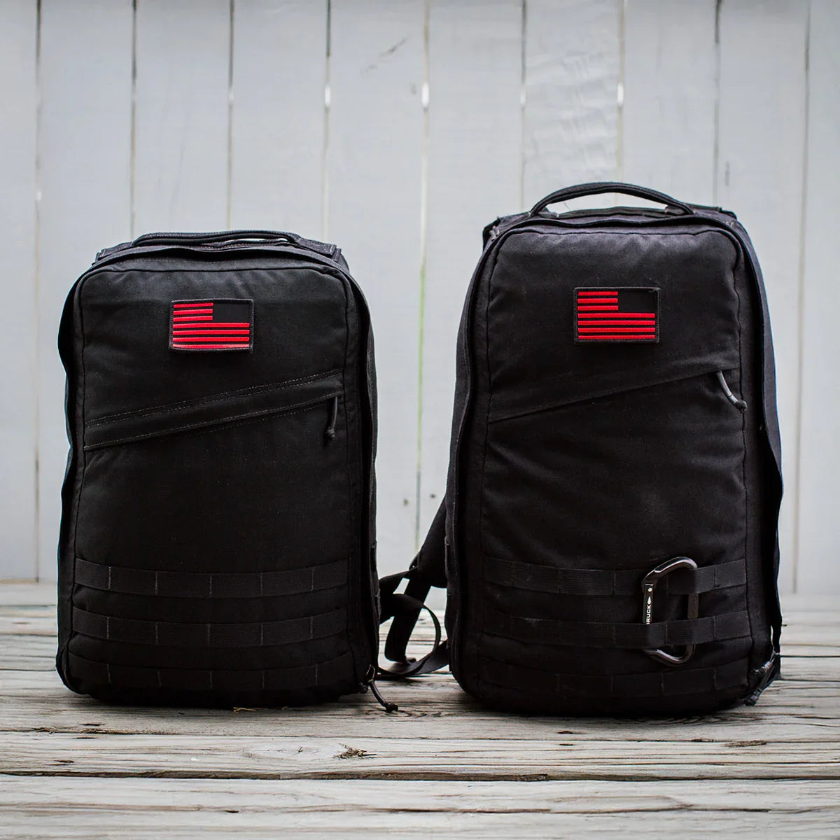 Two black GORUCK rucksacks with red American flag patches on wooden deck, outdoor gear