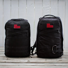 Two black GORUCK rucksacks with red American flag patches on wooden deck, outdoor gear