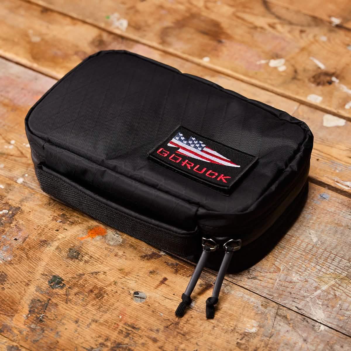 GORUCK black tactical pouch with American flag patch on rustic wooden surface