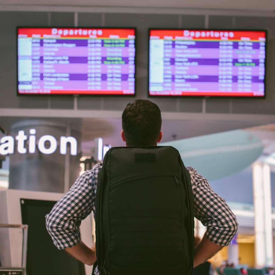 Man with GORUCK backpack at airport, looking at departure boards, rucking gear travel