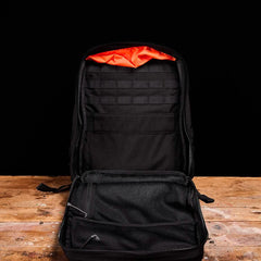 Open GORUCK black rucksack on wooden table, showing orange top liner and interior compartments