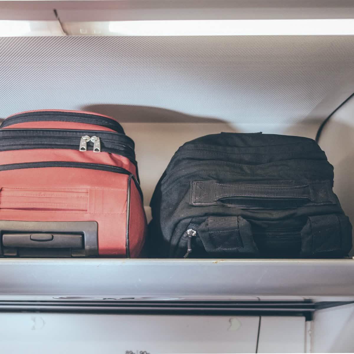 Black GORUCK rucksack and red suitcase in airplane overhead bin