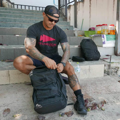 Man wearing GORUCK t-shirt sitting on steps, packing a black GORUCK rucksack outdoors