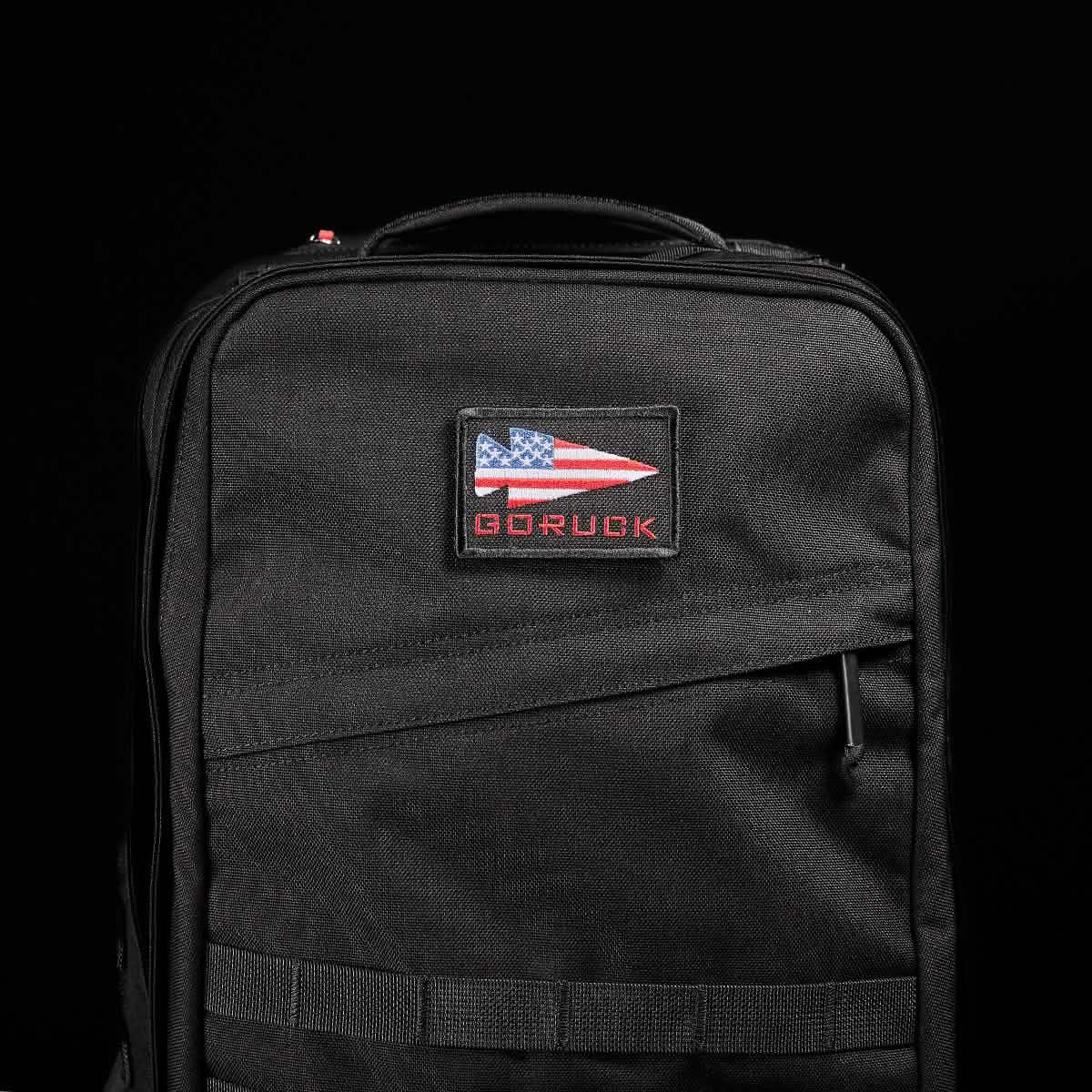 GORUCK black rucksack with American flag patch and zipper, durable rucking gear on black background