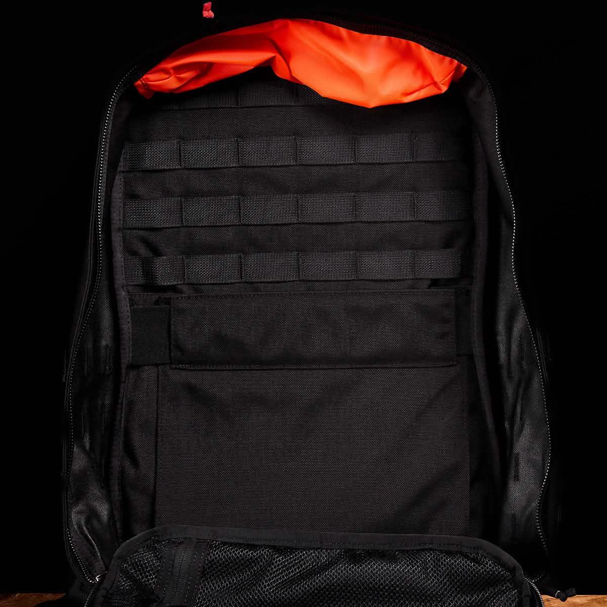 Open GORUCK backpack with black interior, orange lining, and multiple storage compartments