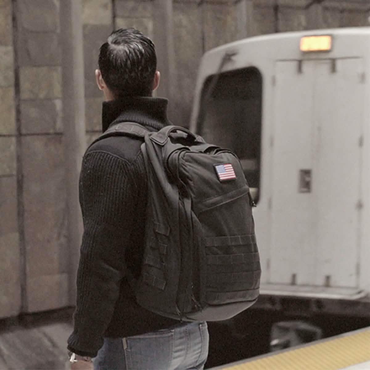 Man wearing GORUCK black rucksack with USA flag patch on subway platform
