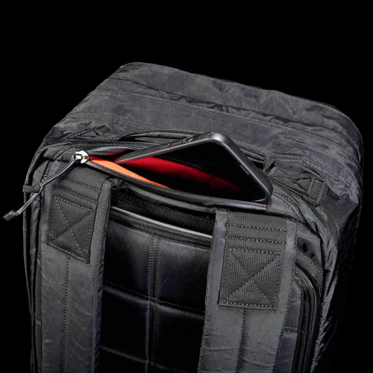 GORUCK black rucksack with visible padded straps and zippered pocket open to reveal a phone