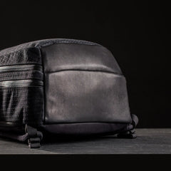 GORUCK black rucking backpack with rugged leather bottom and zippered side pockets on dark background