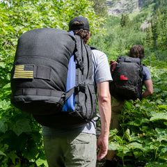 Two people hiking in lush greenery with GORUCK tactical backpacks, outdoor rucking gear