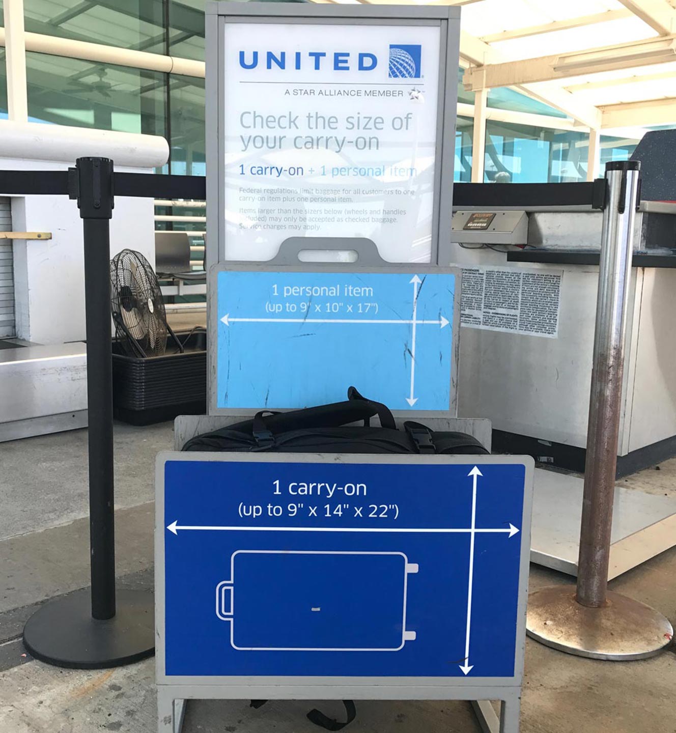 United Airlines carry-on size checker with labeled slots for personal and carry-on items at an airport terminal.