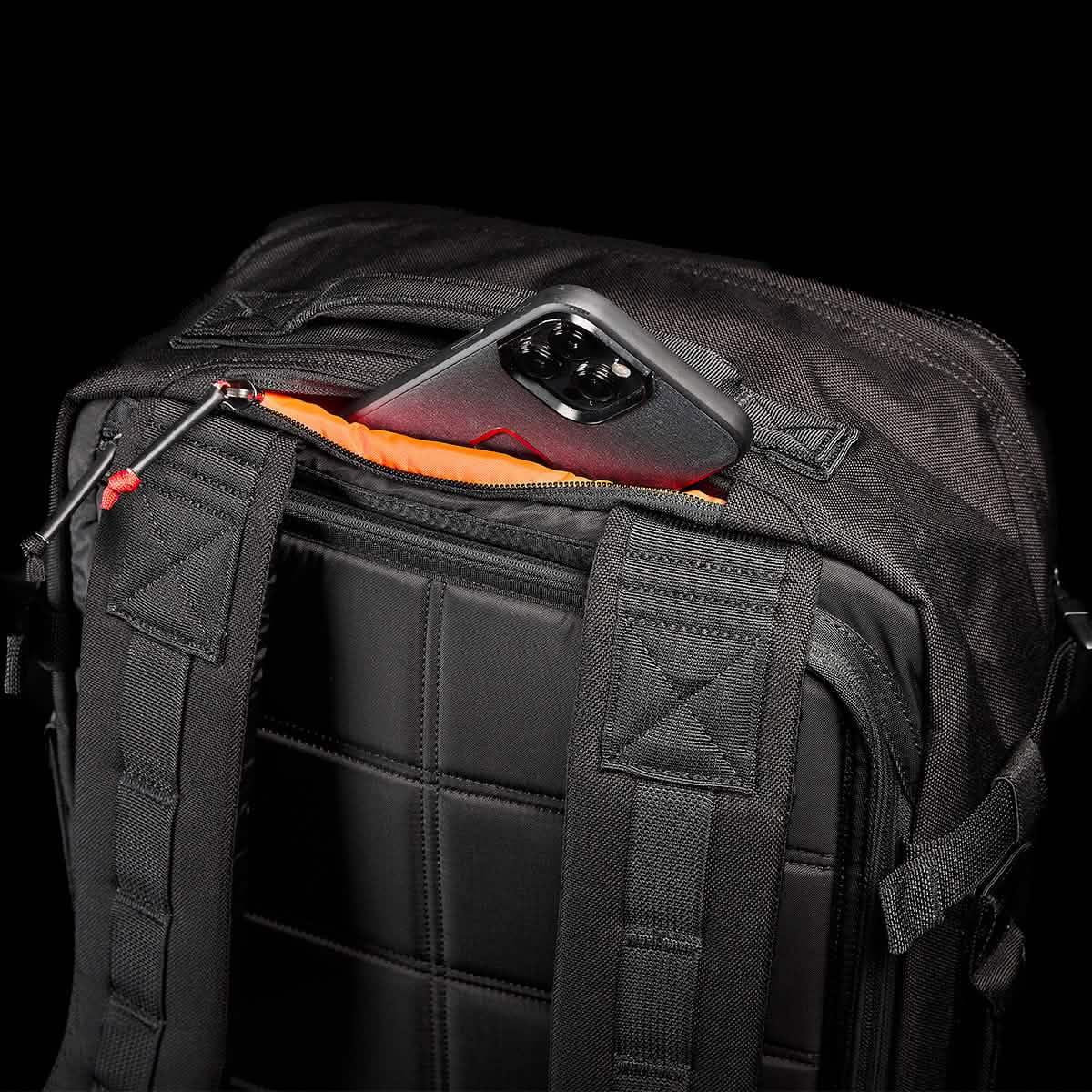 GORUCK black rucksack with padded straps, rear zip pocket open showing a smartphone inside