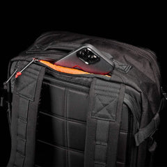 GORUCK black rucksack with padded straps, rear zip pocket open showing a smartphone inside