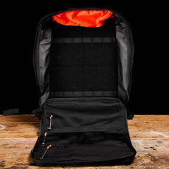 GORUCK GR3 black rucksack open on a wooden table, showing internal compartments and bright orange lining.