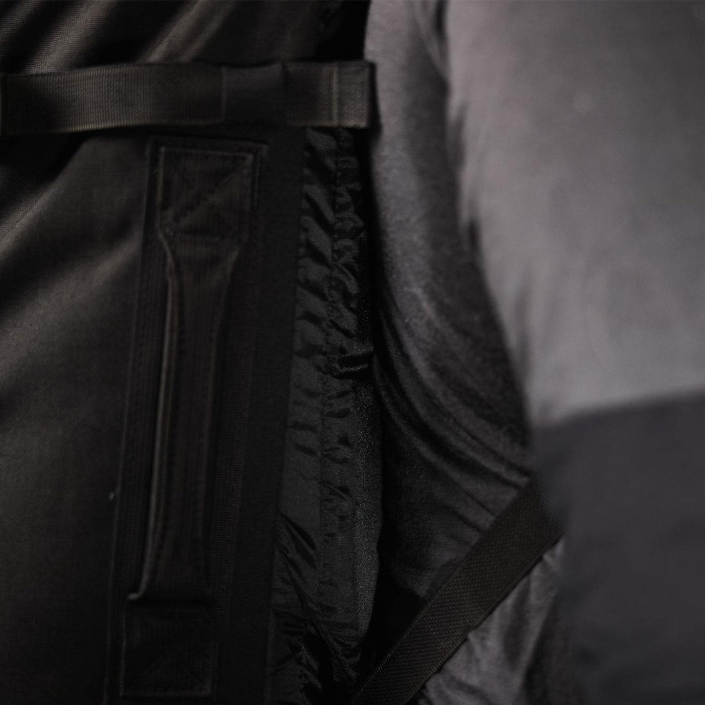 Close-up of black and dark gray fabric layers with straps and stitching details visible.