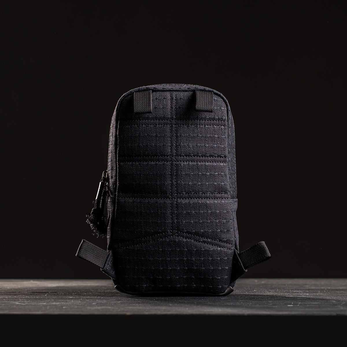 The GRenade x Carryology - GRXC2 Samurai 2.0, a small black tactical pouch with grid stitching and waterproof design, stands upright against a dark background.