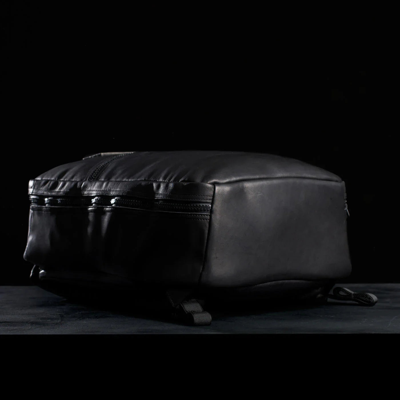 GORUCK black leather backpack with zippers, side view on dark background
