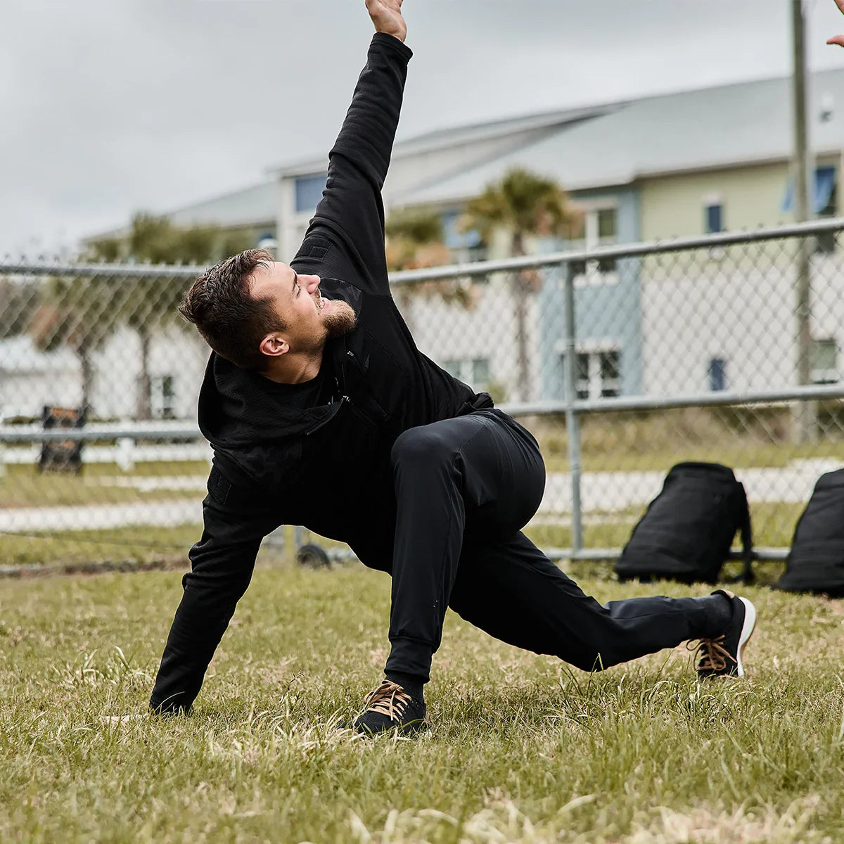 Man stretching outdoors in black GORUCK Grid Fleece Full-Zip jacket, grass field background