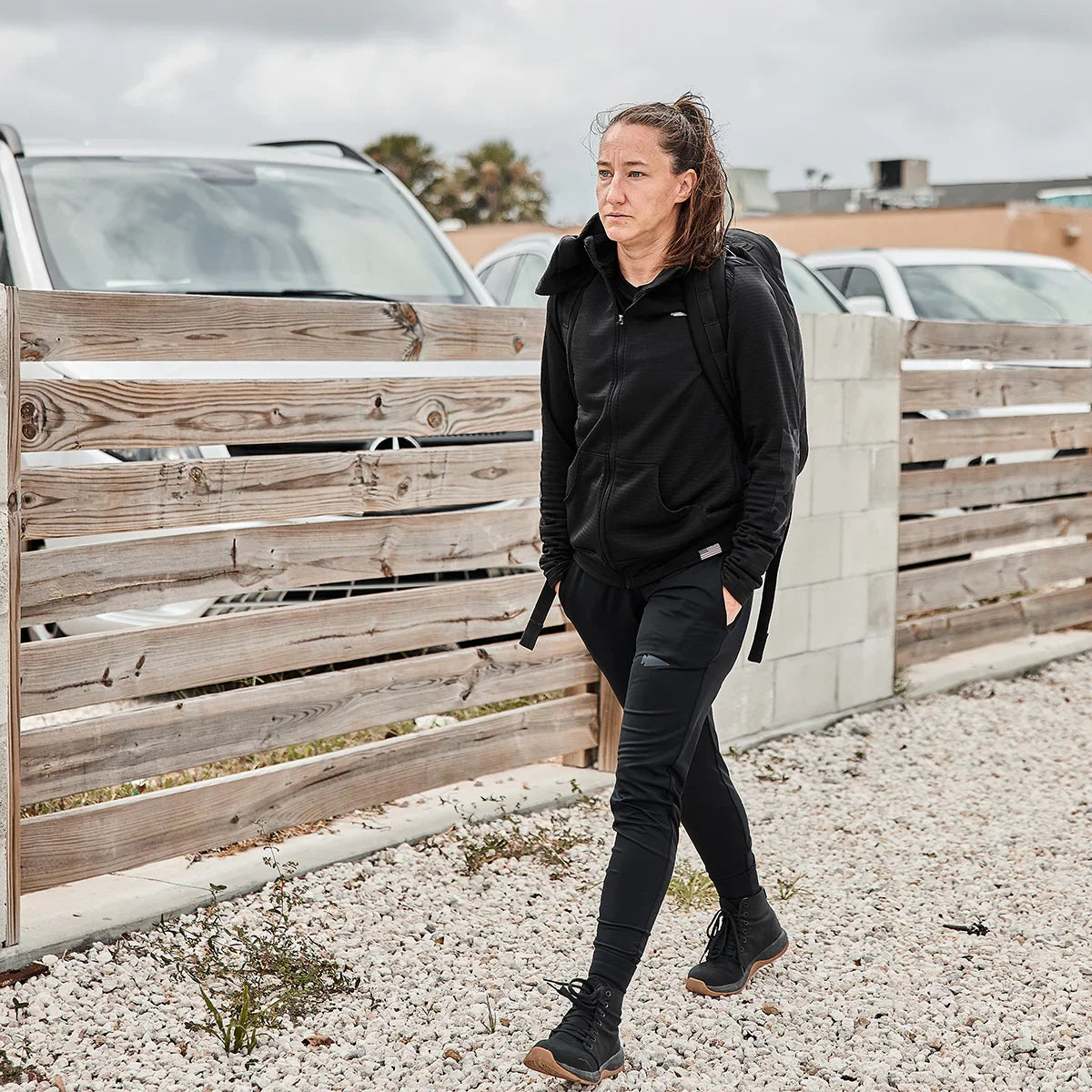 Woman in black GORUCK fleece hoodie and joggers walking outdoors with a rucksack