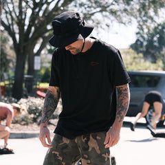 Man wearing black GORUCK boonie hat and camo shorts outdoors during fitness workout
