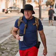 Man wearing GORUCK boonie hat, tactical backpack, and casual gear rucking on a city street