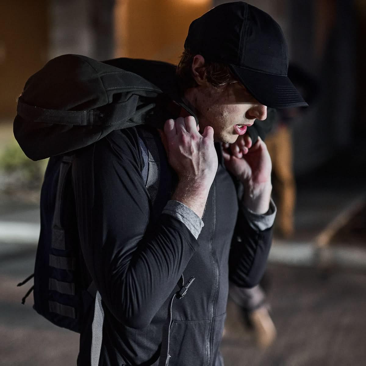 Man wearing black running hat and ruck backpack outdoors at night, GORUCK gear