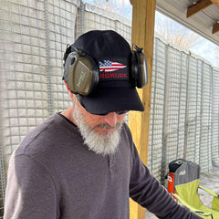 Man wearing GORUCK black hat with American flag patch, earmuffs, and sunglasses outdoors