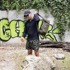 Man outdoors with Ranger Green GORUCK pack, camo shorts, in front of graffiti wall