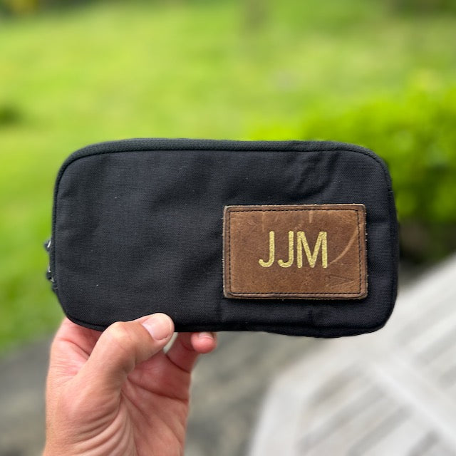 A hand holds the black Sternum Pouch - Cordura with a brown 