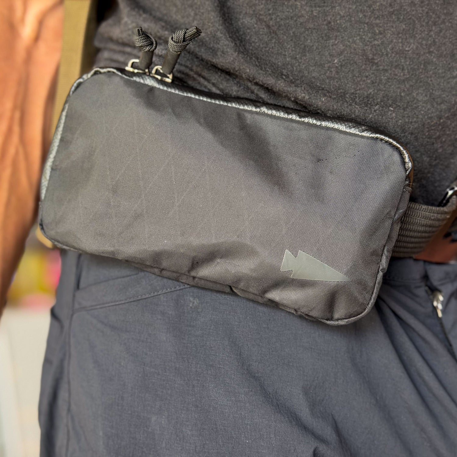 A close-up of the Sternum / Belt Pouch - Waterproof X-PAC, a black zippered pouch worn on a belt for easy access to essentials—perfect for rucking activities.