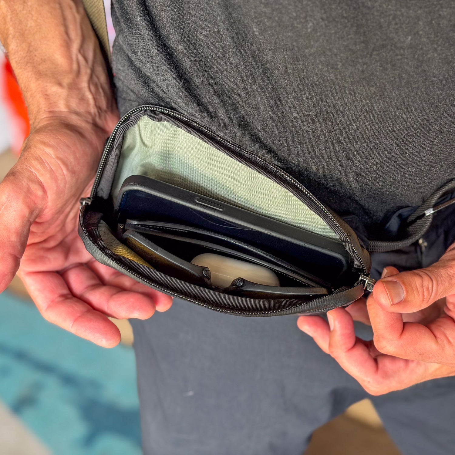 A person holds an open Sternum / Belt Pouch - Waterproof X-PAC in black, with a phone and sunglasses inside for easy access.