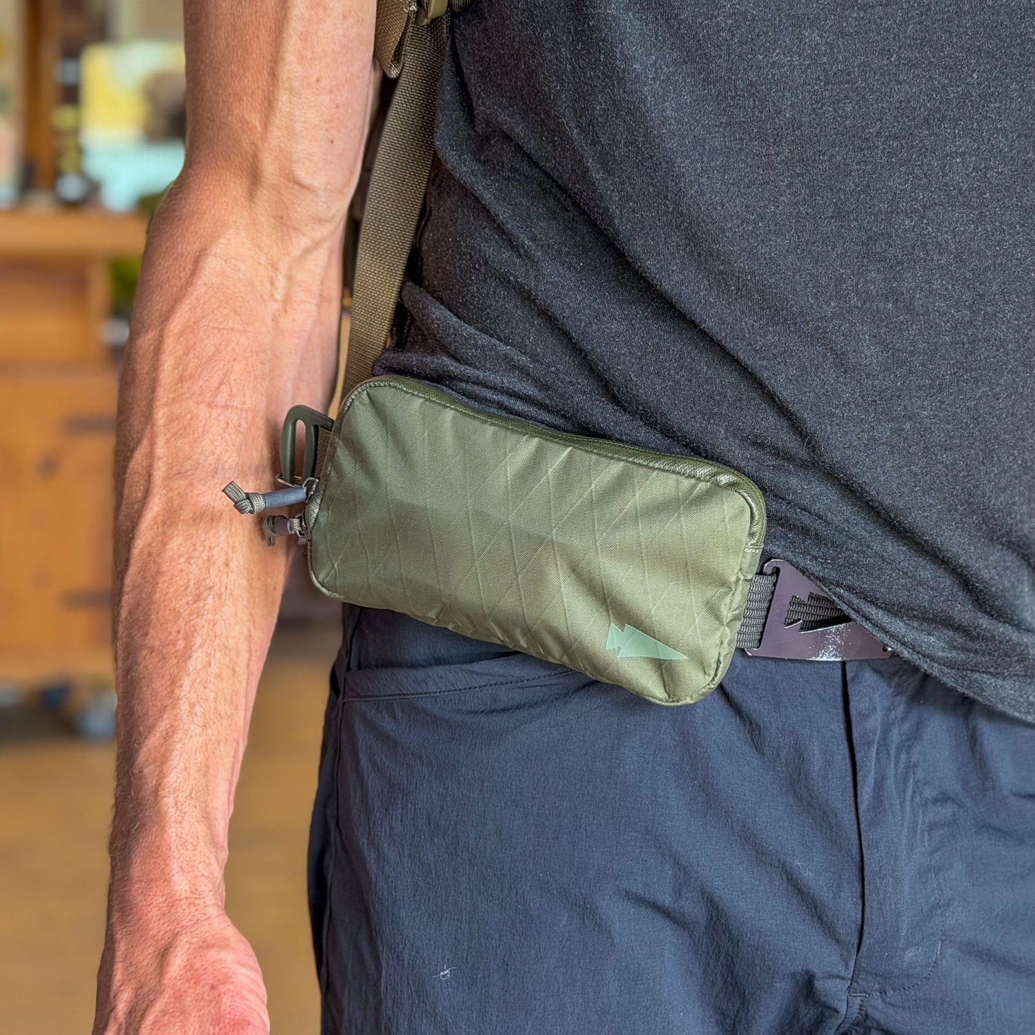 A person sports a small green Sternum / Belt Pouch - Waterproof X-PAC strapped to their waist over dark clothing, adding a functional touch to their rucking gear.
