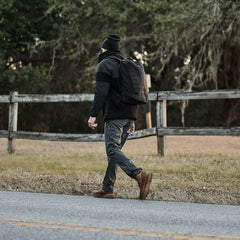 Man rucking with GORUCK backpack outdoors near wooden fence, wearing outdoor gear