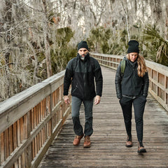 Two people wearing GORUCK gear hiking on a wooden boardwalk in a forested area