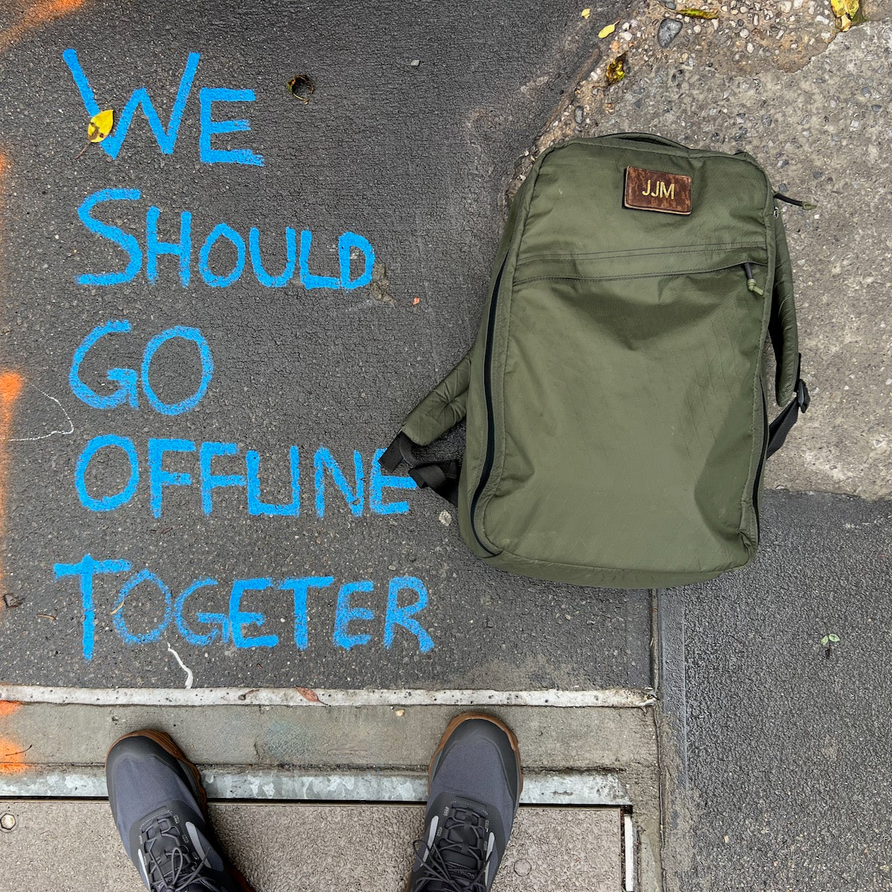 Patch - Custom Leather Monogram backpack in olive green rests on pavement with a personalized leather patch. Blue chalk text says, 