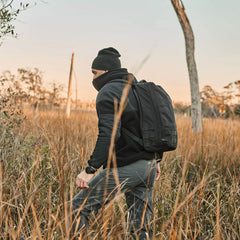 Man rucking outdoors in field at sunset wearing GORUCK backpack, beanie, and jacket