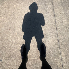 Shadow of a person wearing shorts, shoes, and the Men's USA Sun Hoodie - Full-Zip - ToughMesh, with their feet visible at the bottom, cast on the pavement.