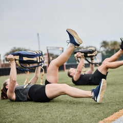 Two people rucking with GORUCK sandbags while exercising on a turf field outdoors
