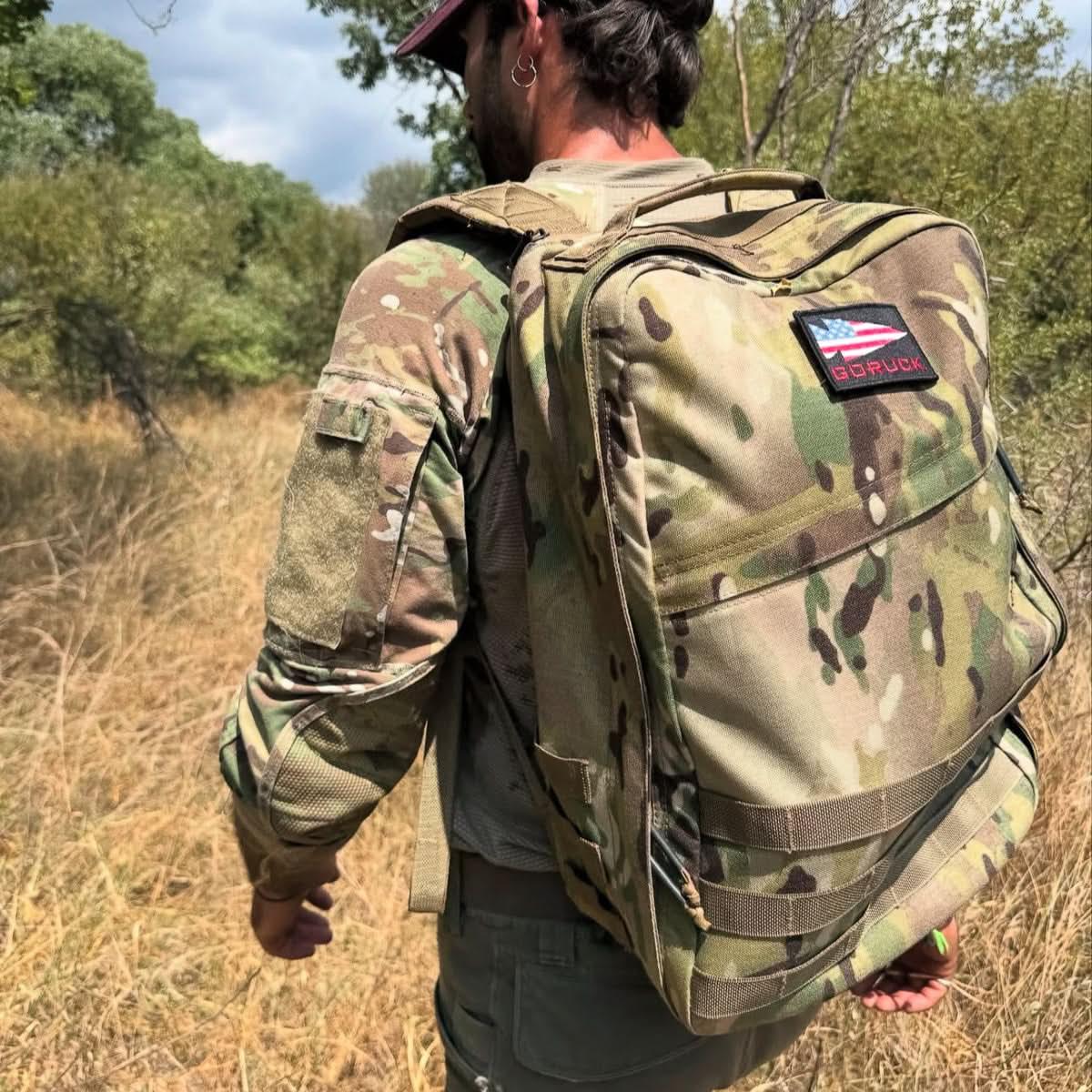 Man rucking outdoors wearing GORUCK camo backpack and tactical gear in grassy field