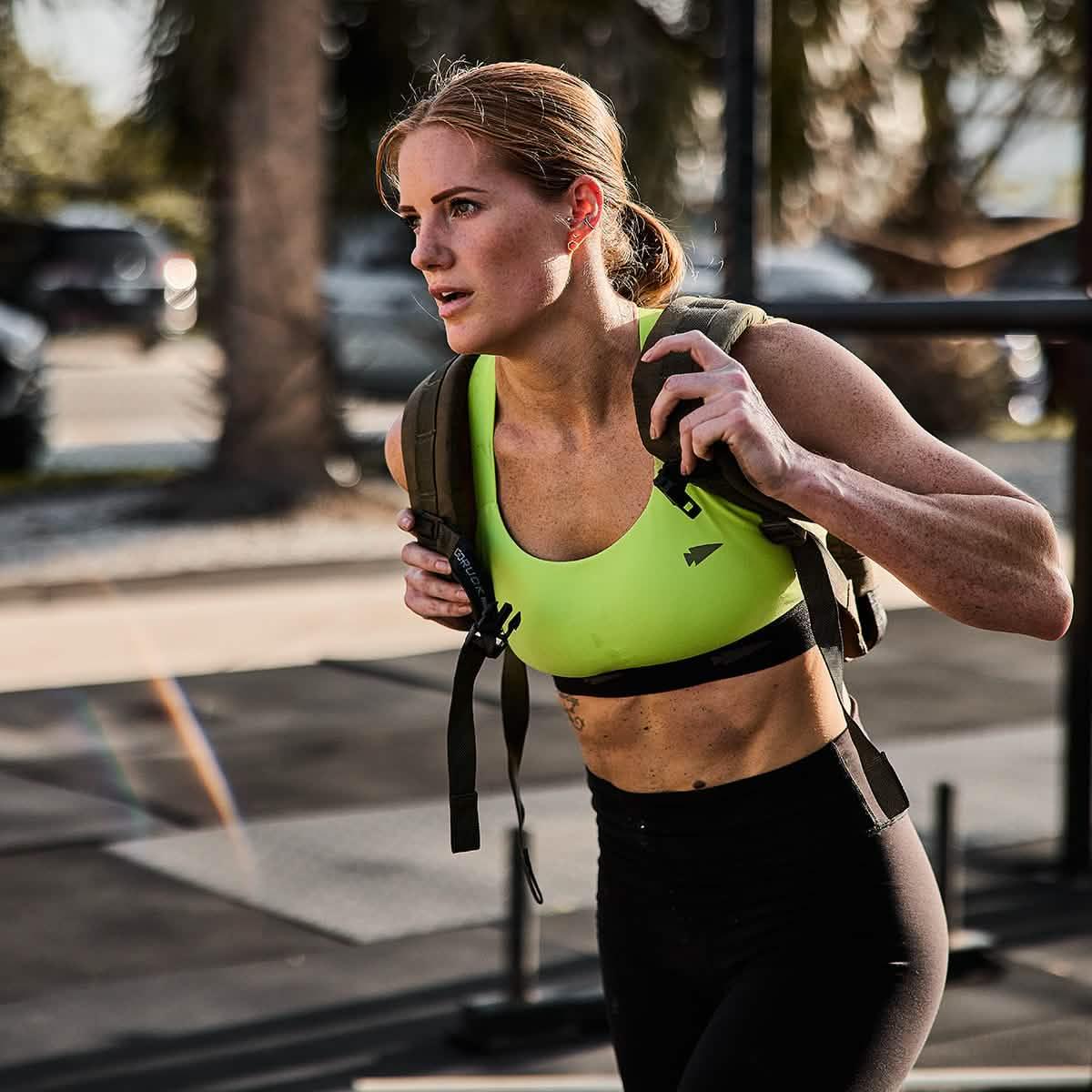 Athletic woman rucking with GORUCK backpack outdoors, wearing neon sports bra and black leggings