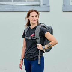 A woman wearing a black t-shirt, blue pants, and a watch stands outside with the GR2 - Cordura travel backpack.